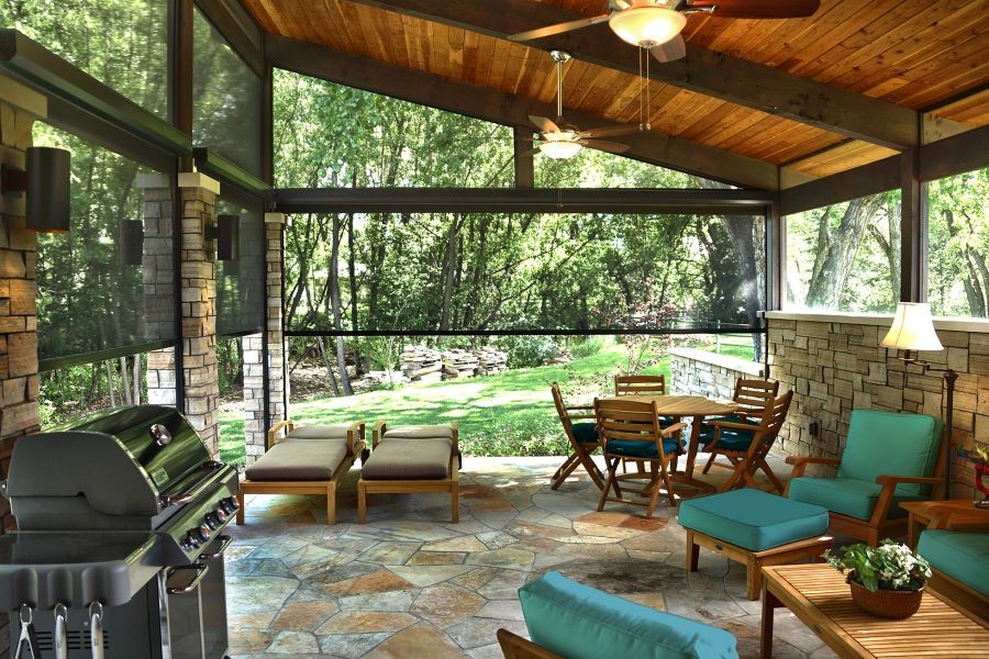 Outdoor motorized shades halfway lowered around a patio with fans, seating areas, and a grill.