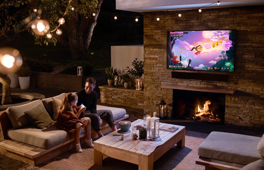 A father and daughter enjoy a show under the stars on a TV mounted above an outdoor fireplace.